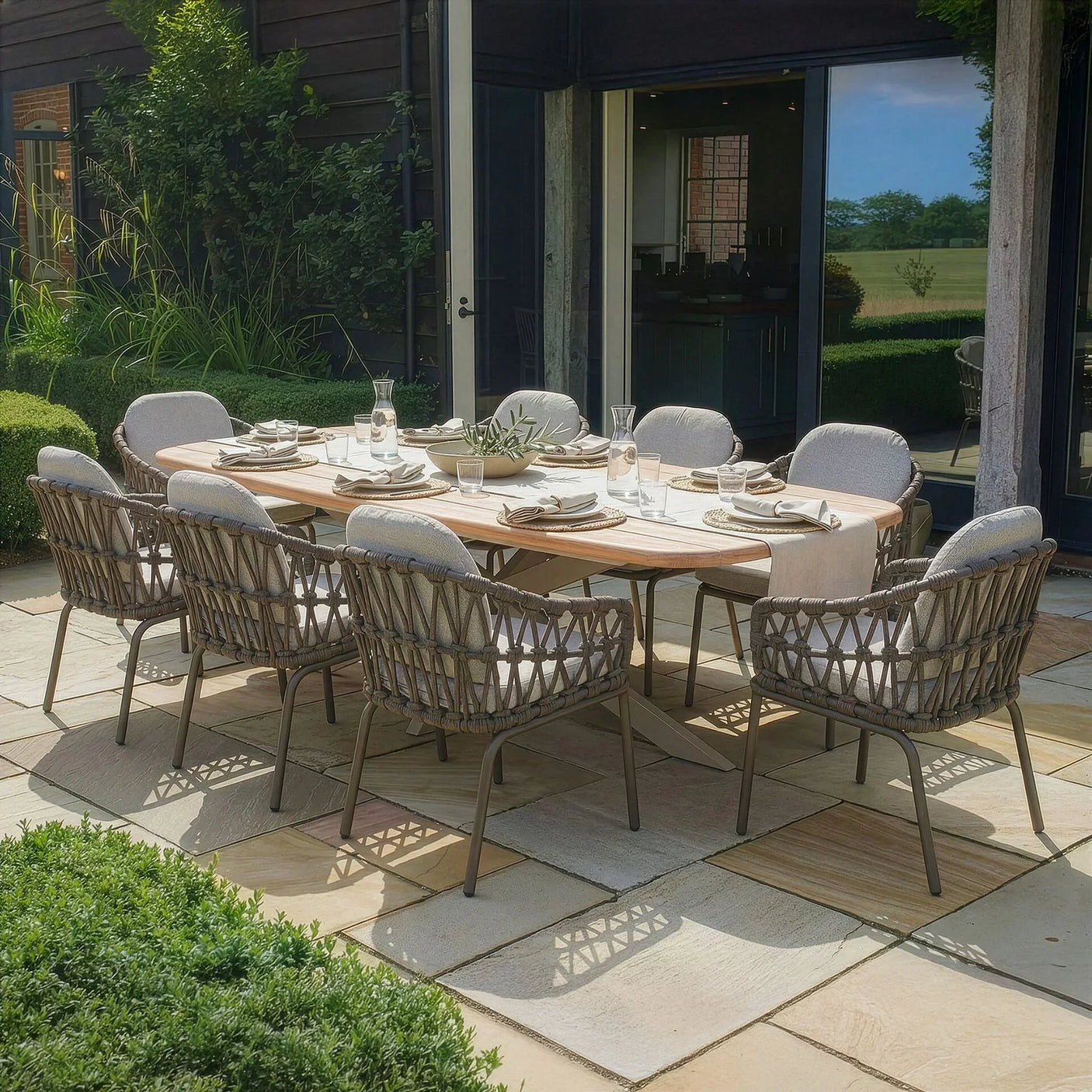 Rattan outdoor dining set with eight cushioned chairs and wooden table on stone patio