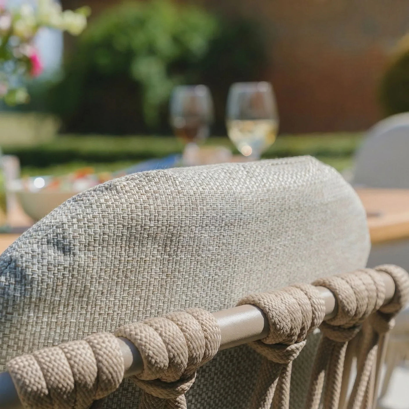 Closeup of woven outdoor dining chair with rope detail, garden table setting in background