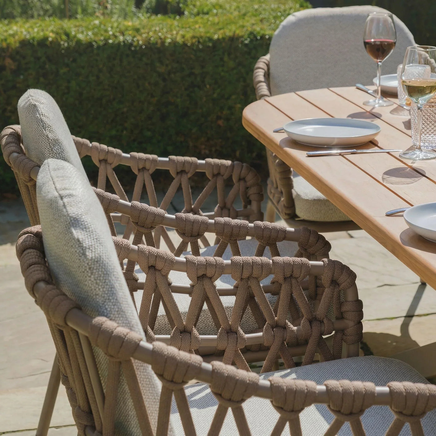 Outdoor rope dining chairs with beige cushions around wooden garden table set