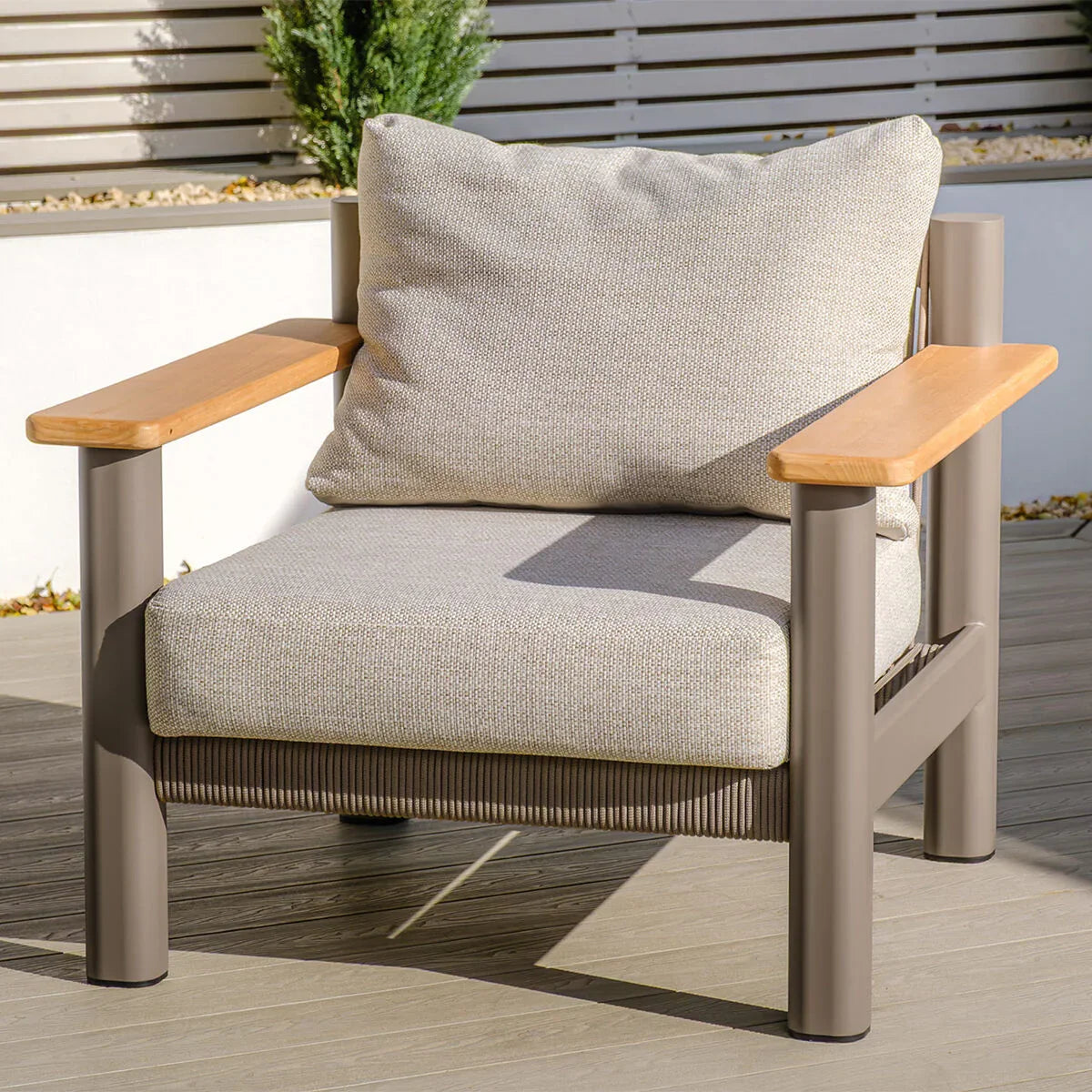Outdoor armchair with beige cushions, taupe metal frame and wooden armrests on decking