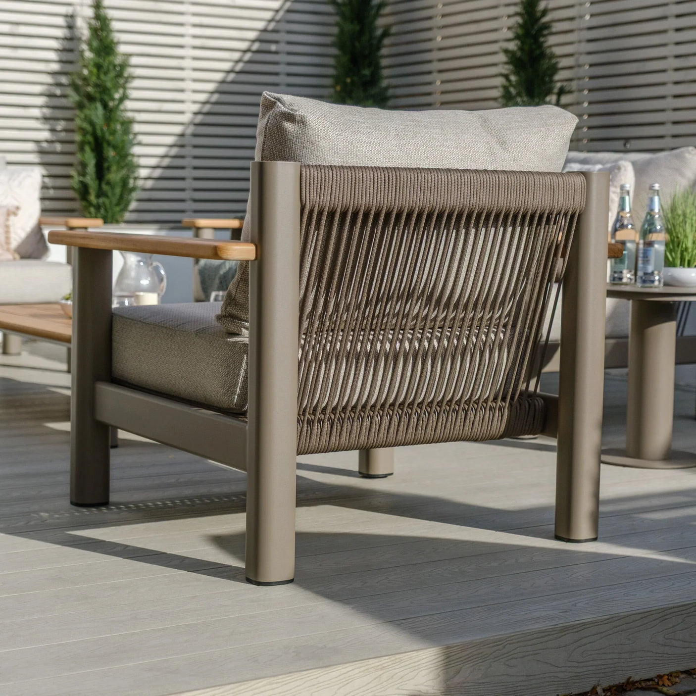 Modern outdoor lounge chair with rope back, beige cushions, and wooden armrests on patio