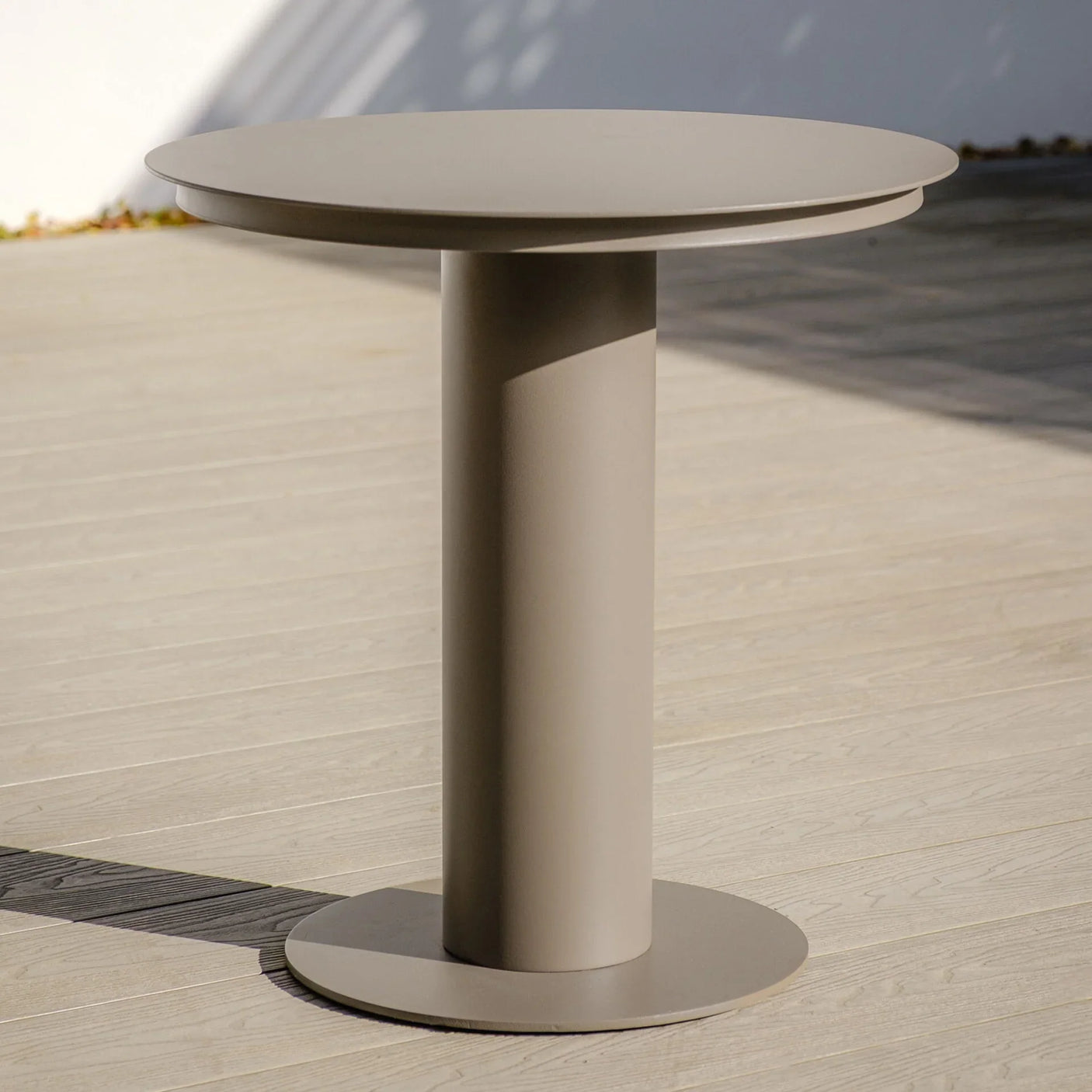 Round taupe outdoor dining table with pedestal base on light wood decking