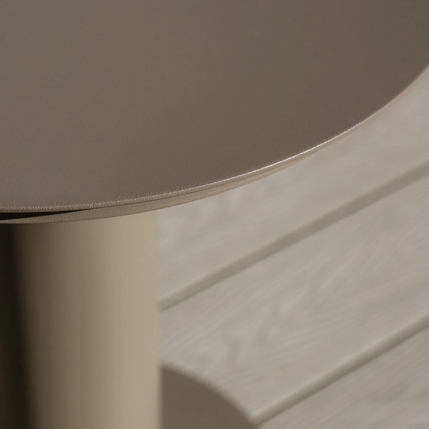 Round taupe metal side table close-up with smooth top and cylindrical base on decking