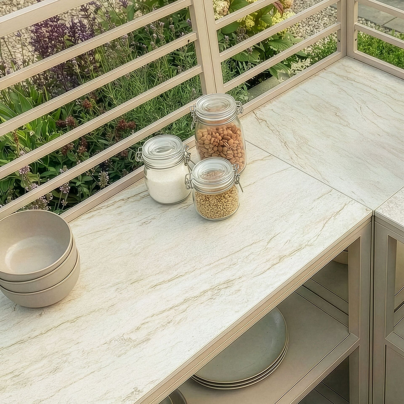 Outdoor kitchen worktop with beige stone surface, glass storage jars, and stacked bowls