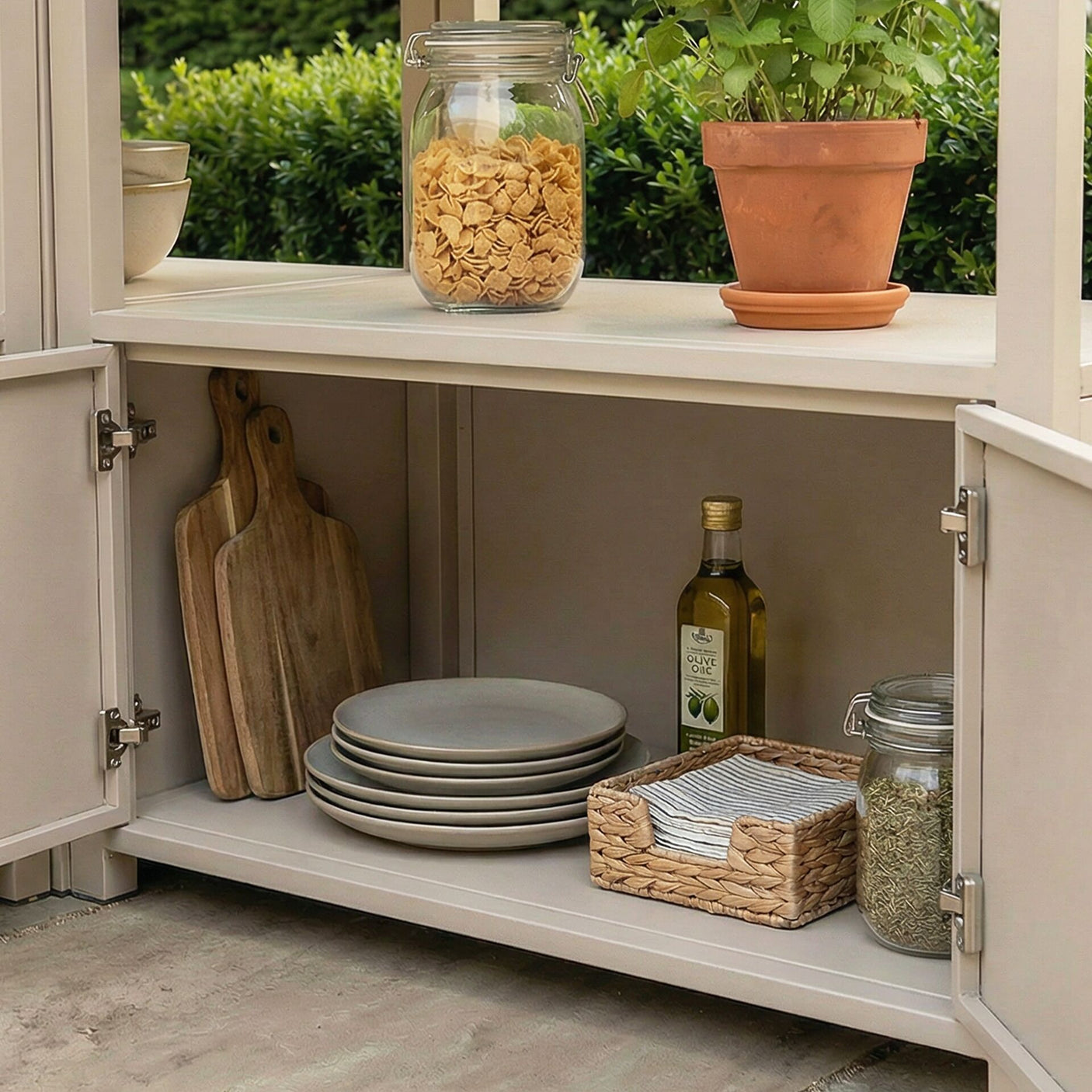 Outdoor kitchen storage unit with wooden boards, plates, olive oil, and glass jars on shelves