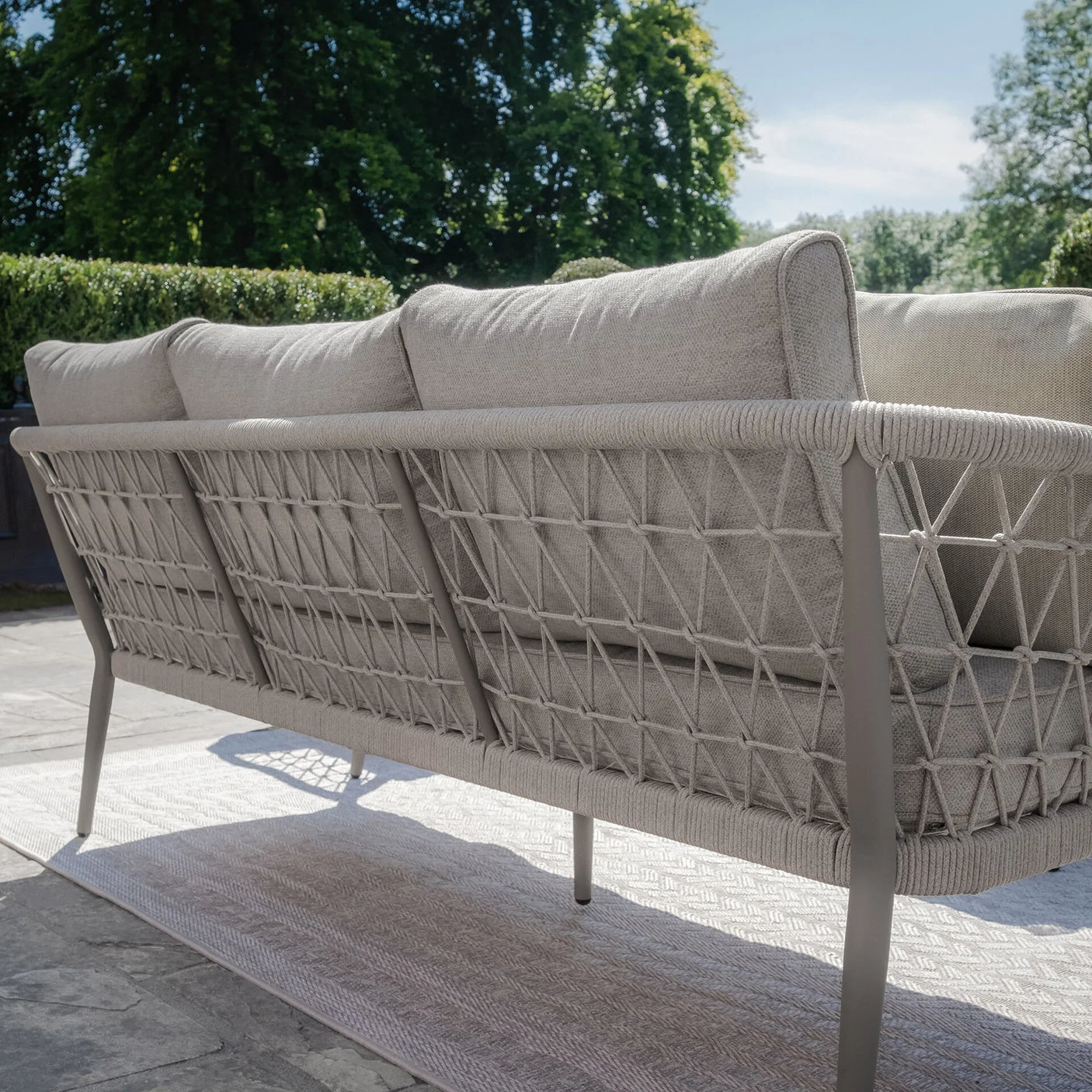 Beige outdoor sofa with rope woven backrest and metal frame on patio in garden setting