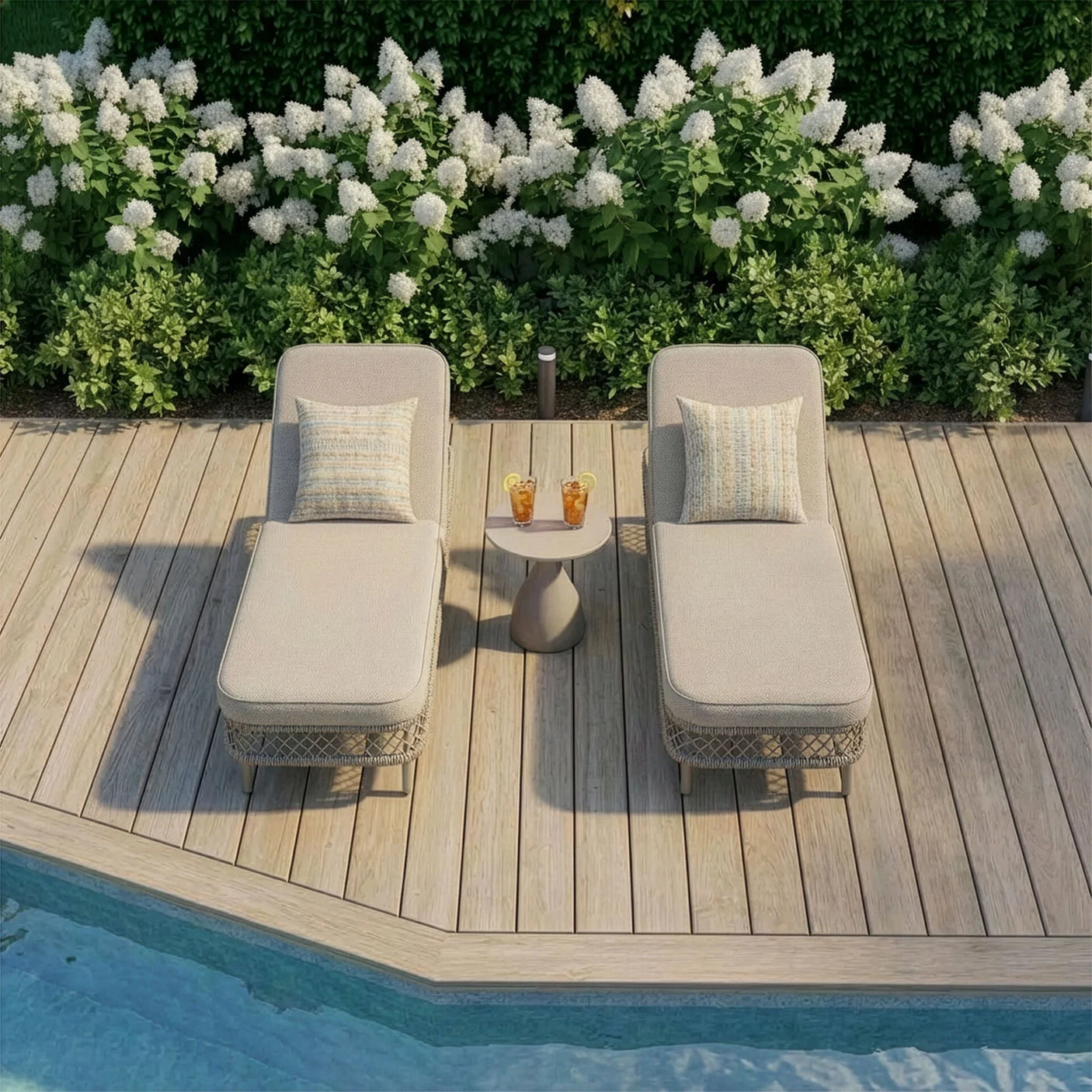 Beige rattan sun lounger set with side table by pool on wooden deck with floral backdrop