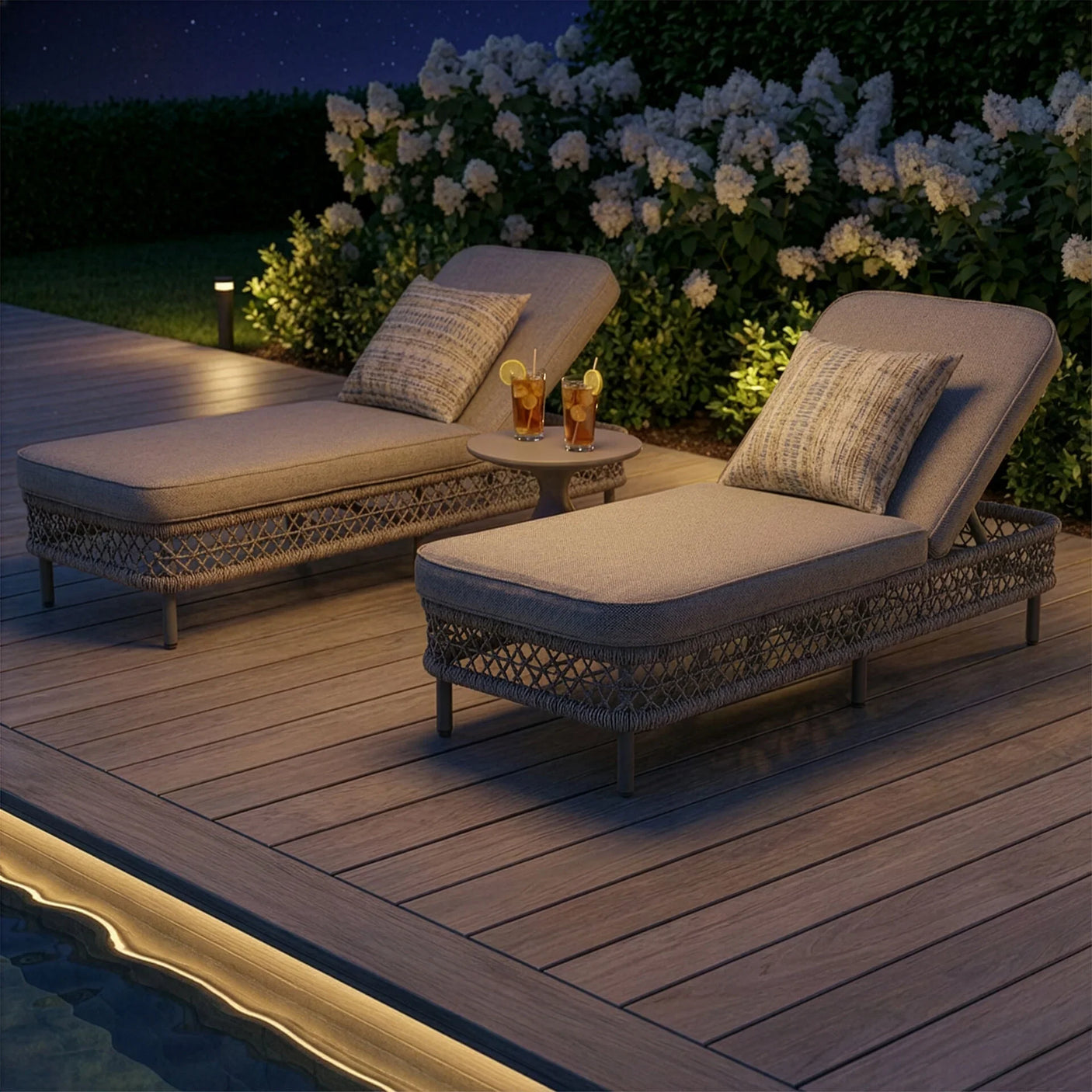 Rattan sun lounger set with cushions and side table on wooden decking near garden pool