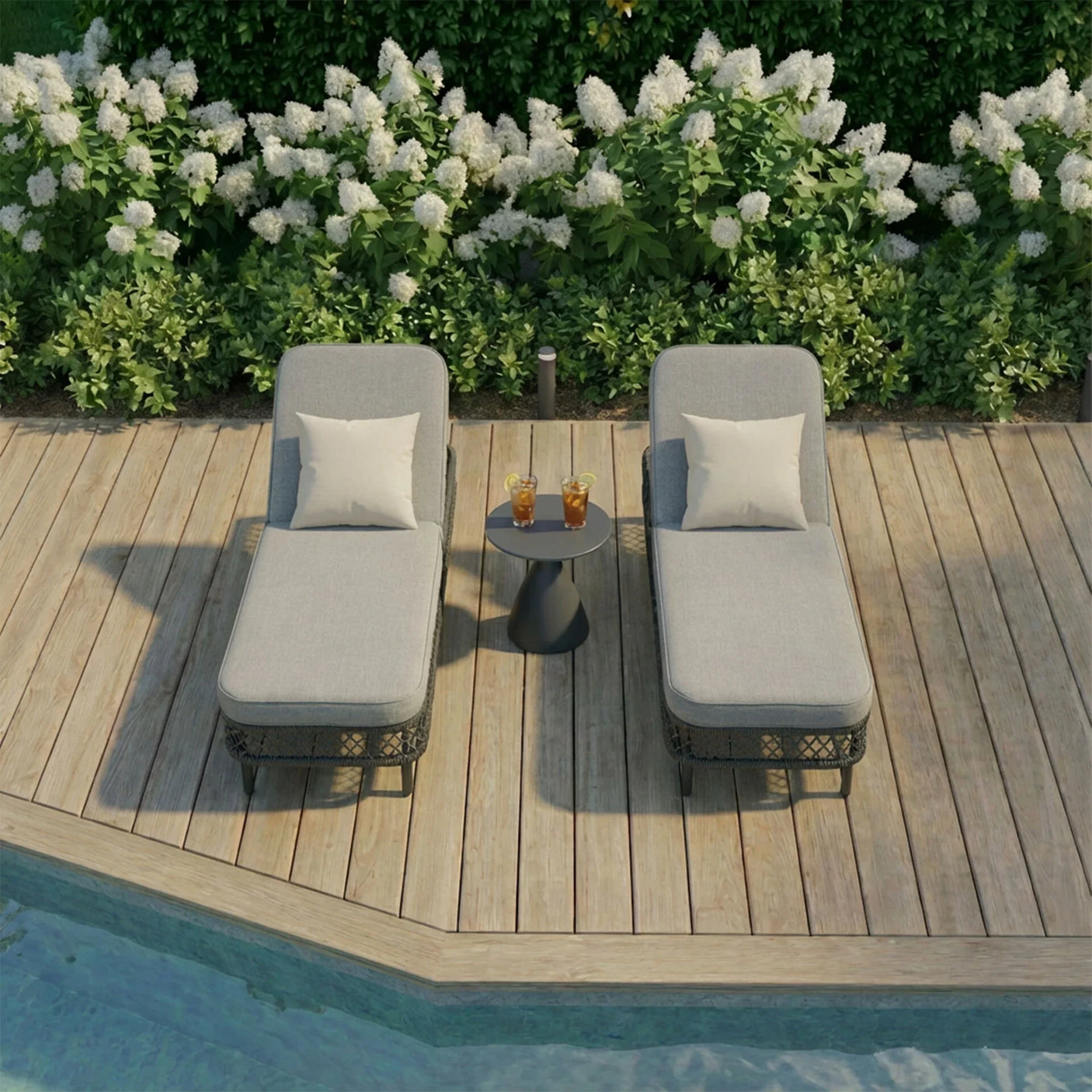 Rattan sun loungers with grey cushions and side table on wooden decking by pool