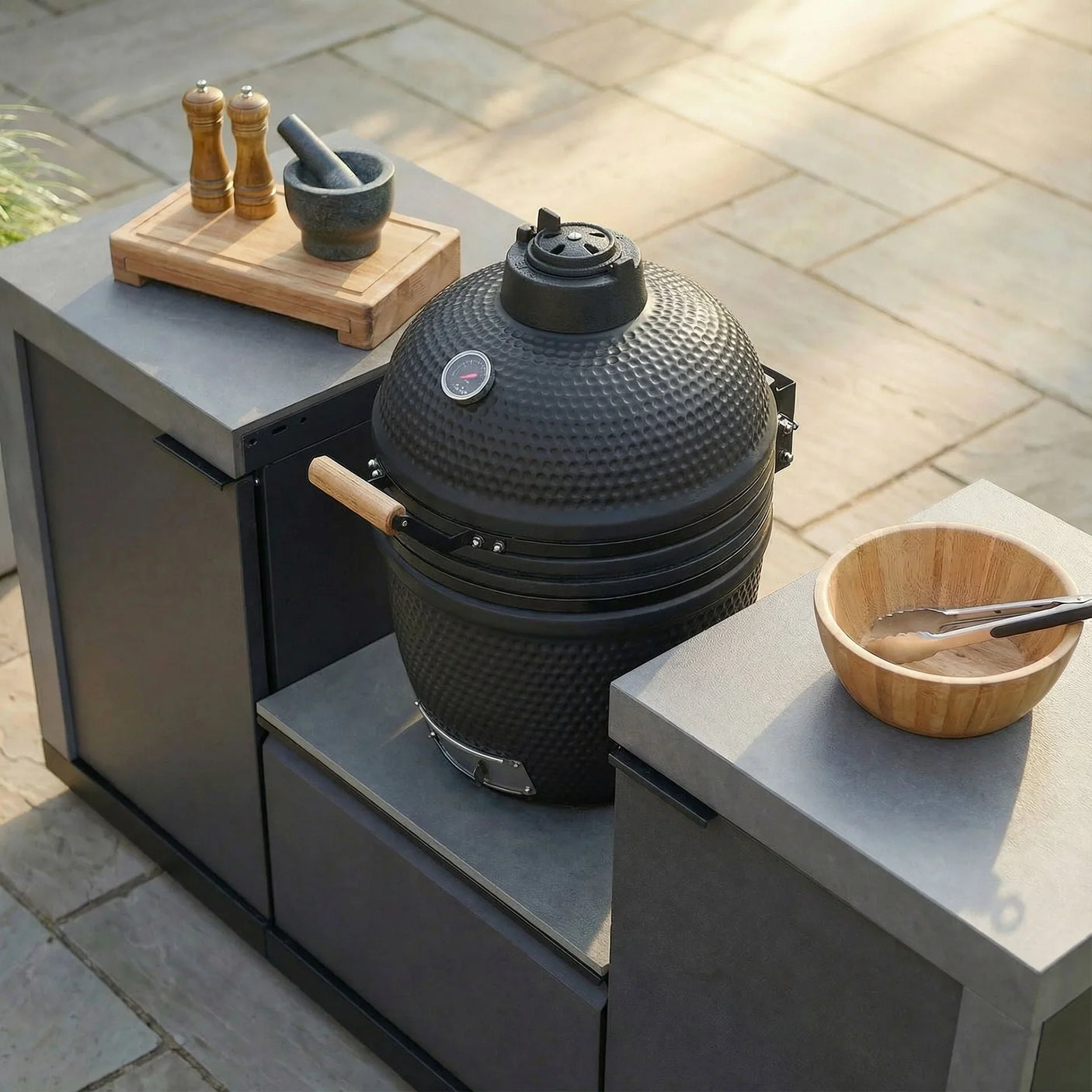 Black outdoor kamado grill in modern garden kitchen with prep counter and utensils