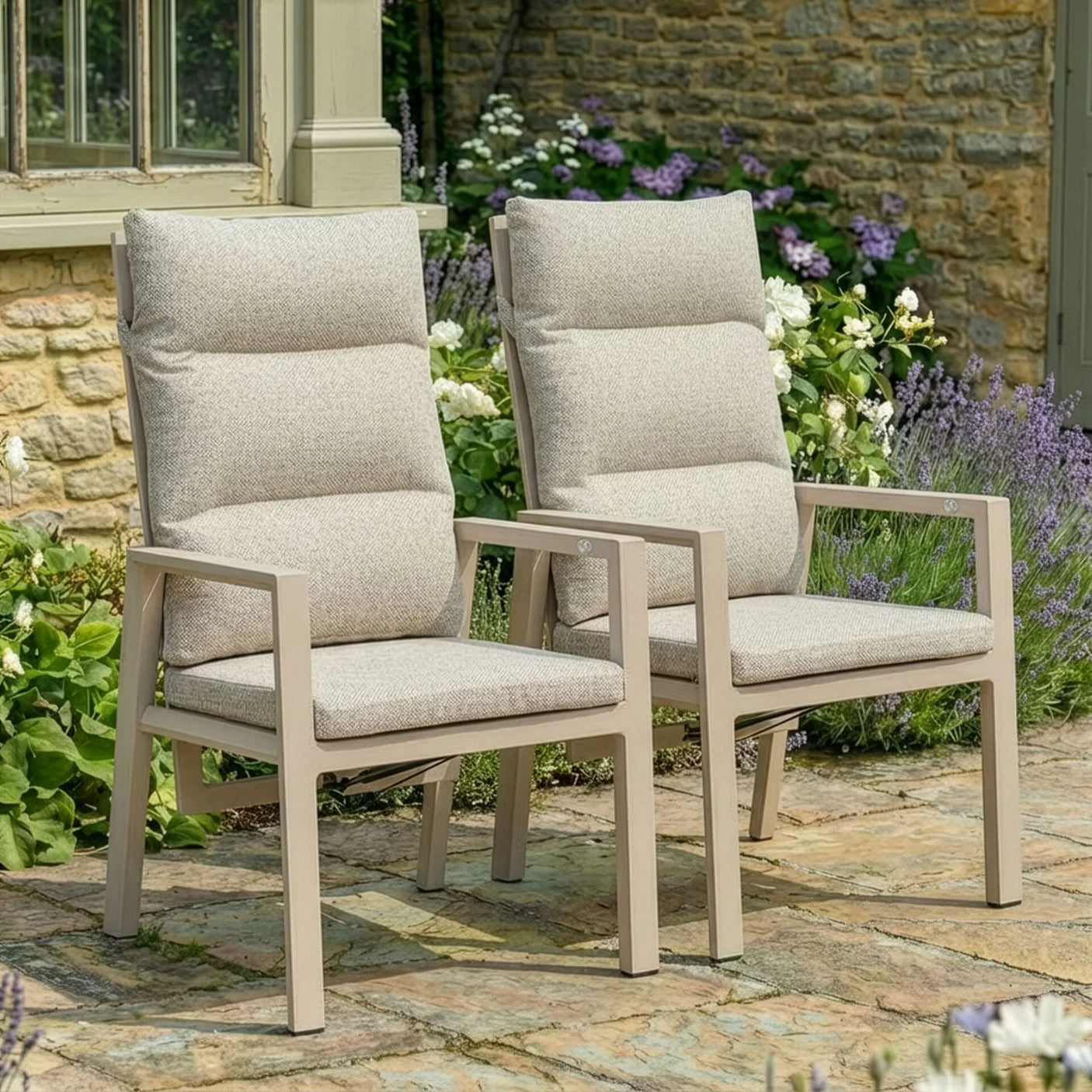 Beige cushioned garden dining chairs on stone patio with flowers and stone wall background