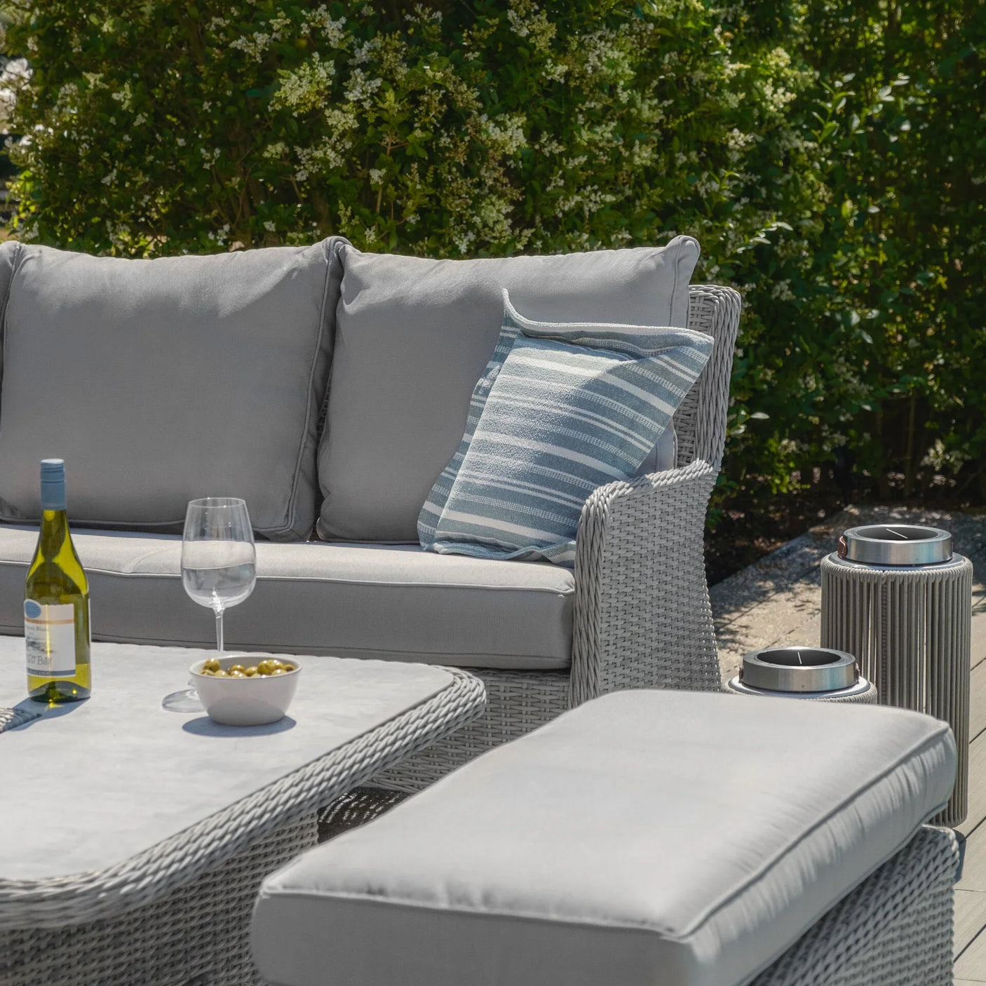 Grey rattan outdoor sofa set with cushions, striped pillow, coffee table and bottle of wine