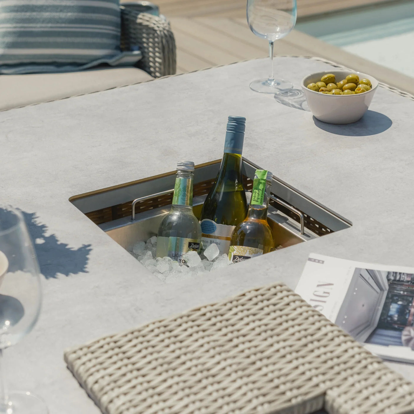 Outdoor dining table with ice bucket, wine bottles, glass, olives and wicker placemat