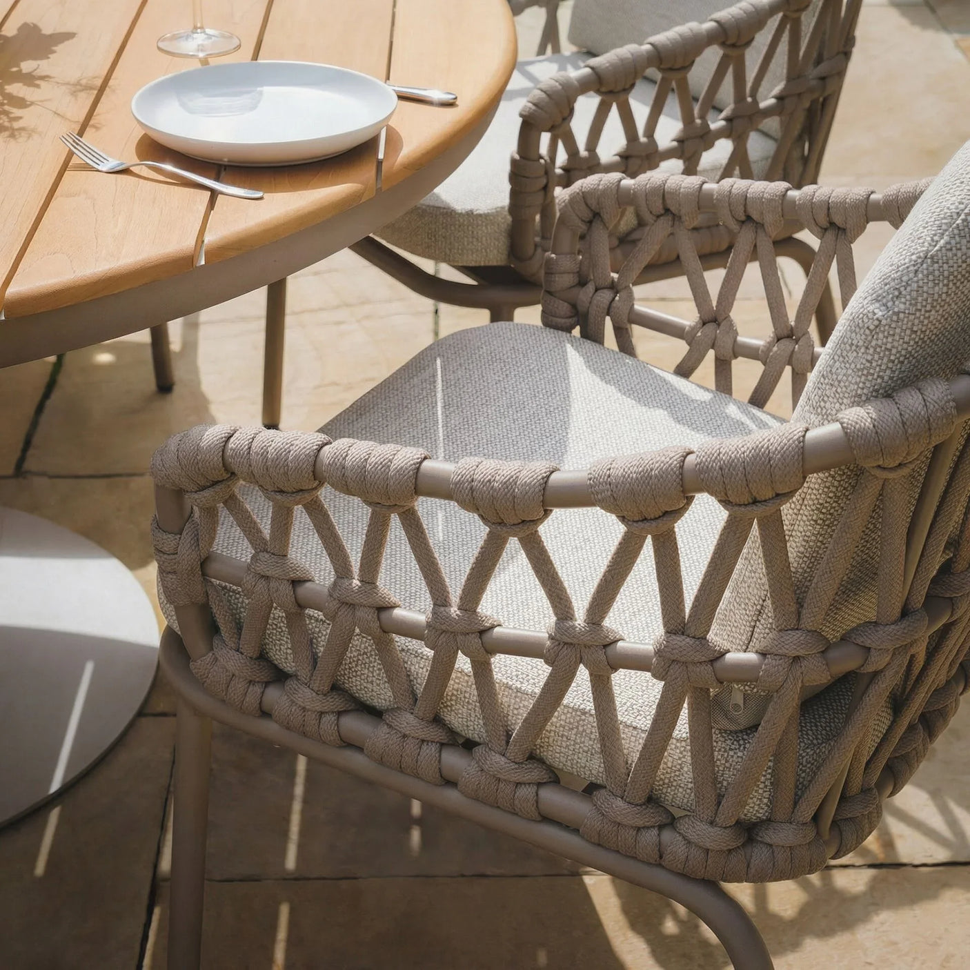 Outdoor rope dining chair with light grey cushion beside round wooden table on patio