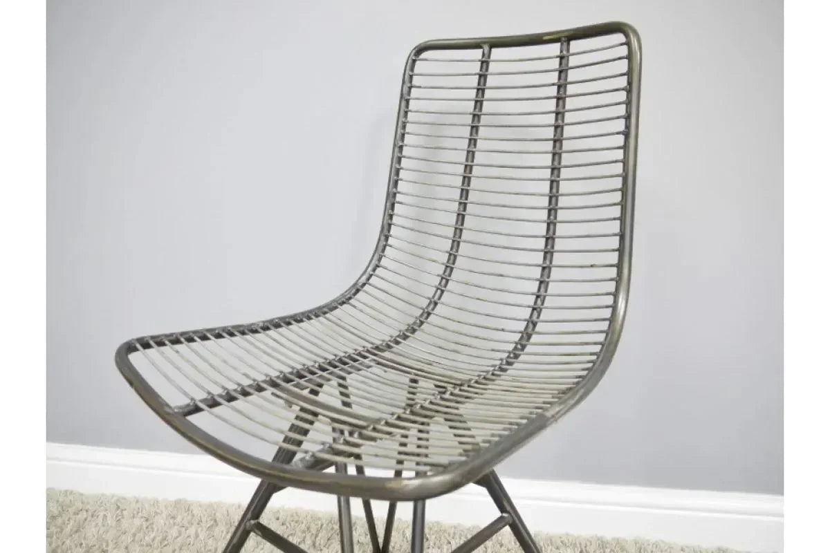 Modern metal dining chair with open wire design and angled legs against grey wall