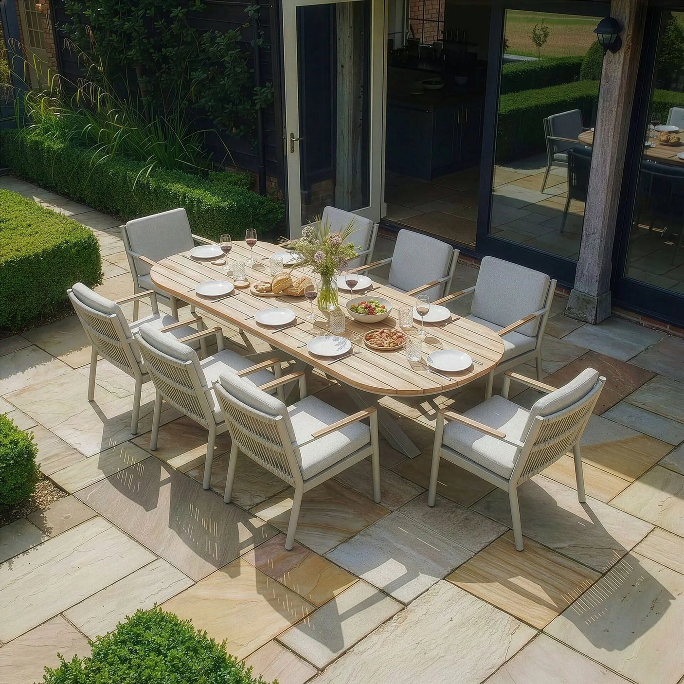 Outdoor dining set with eight cushioned chairs and wooden table arranged on stone patio