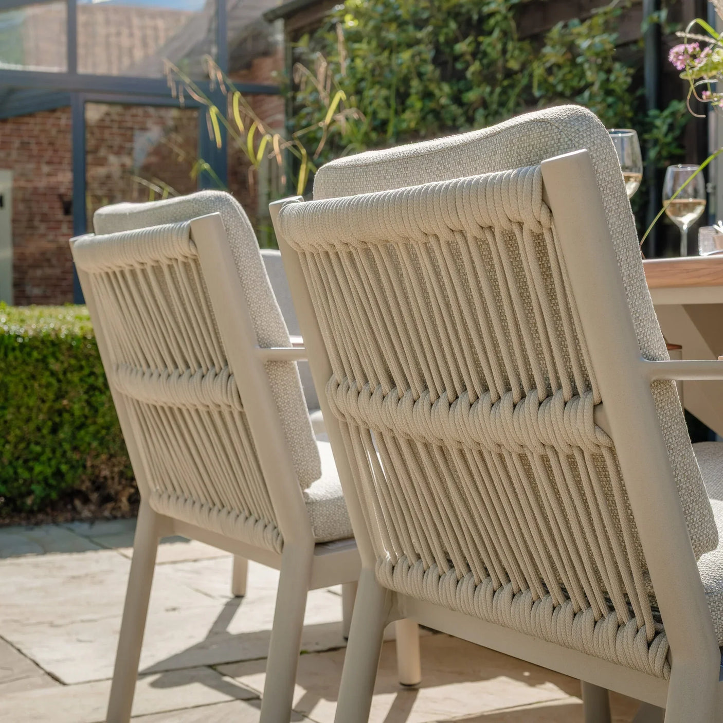 Outdoor dining chairs with beige rope weave backs and cushions on a patio