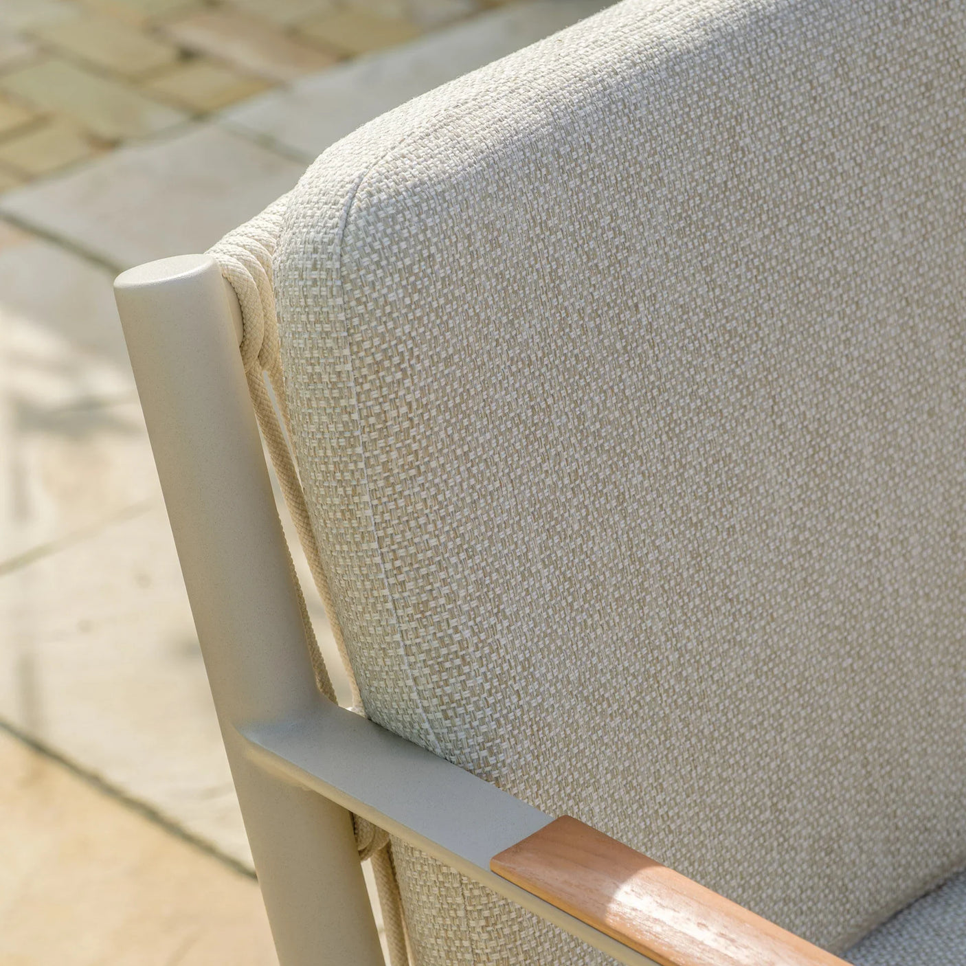 Close-up of beige outdoor chair with textured fabric cushion and metal frame armrest