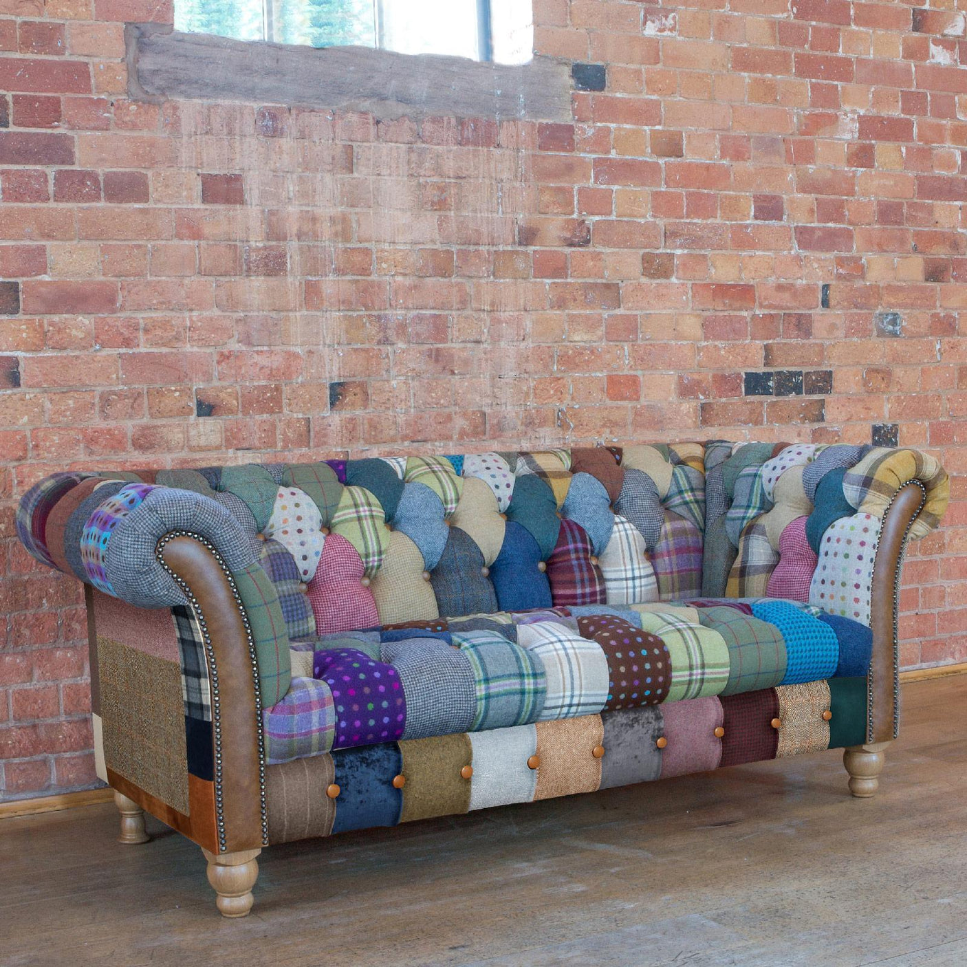 Patchwork fabric Chesterfield sofa with wooden legs against exposed brick wall