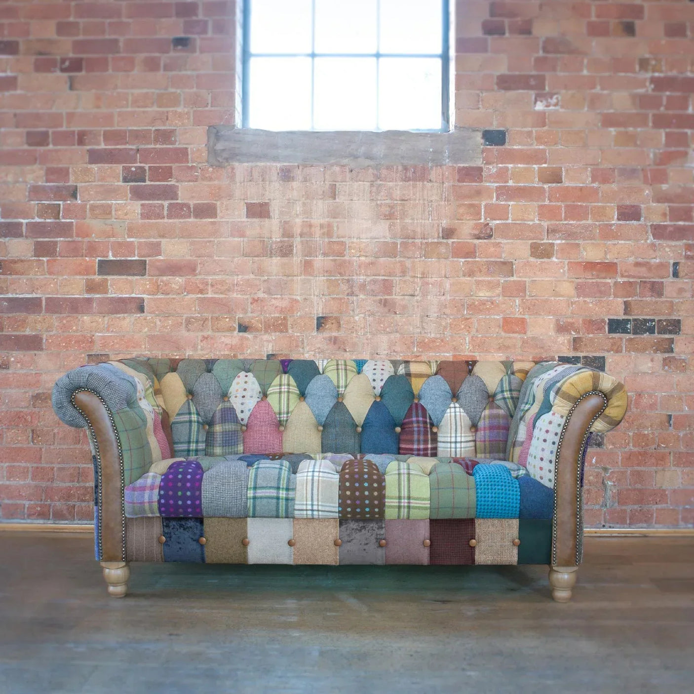 Patchwork Chesterfield sofa with wooden legs against exposed brick wall