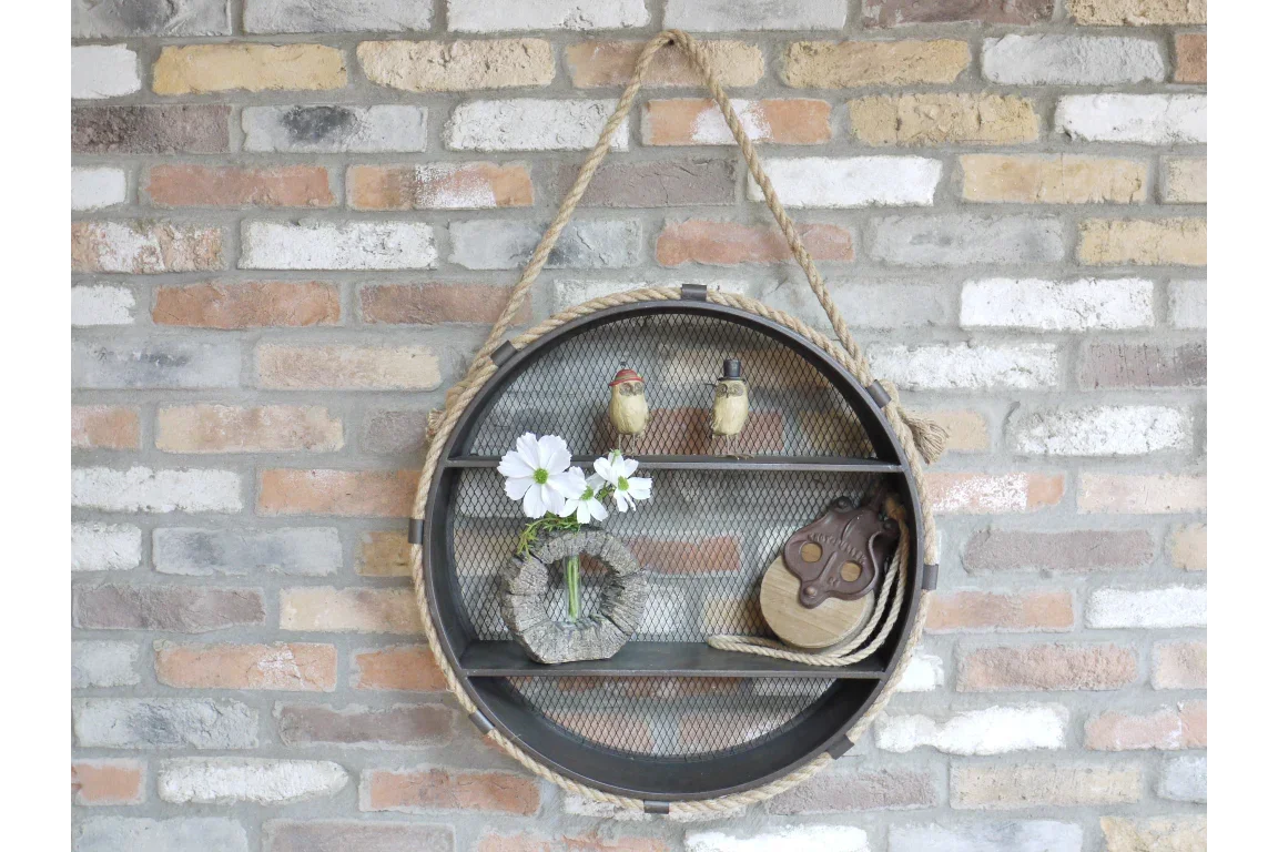 Round metal wall shelf with rope detail holding ornaments and small vase against brick wall