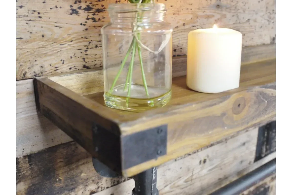 Industrial wood and metal shelf with a glass vase and lit candle against rustic wall