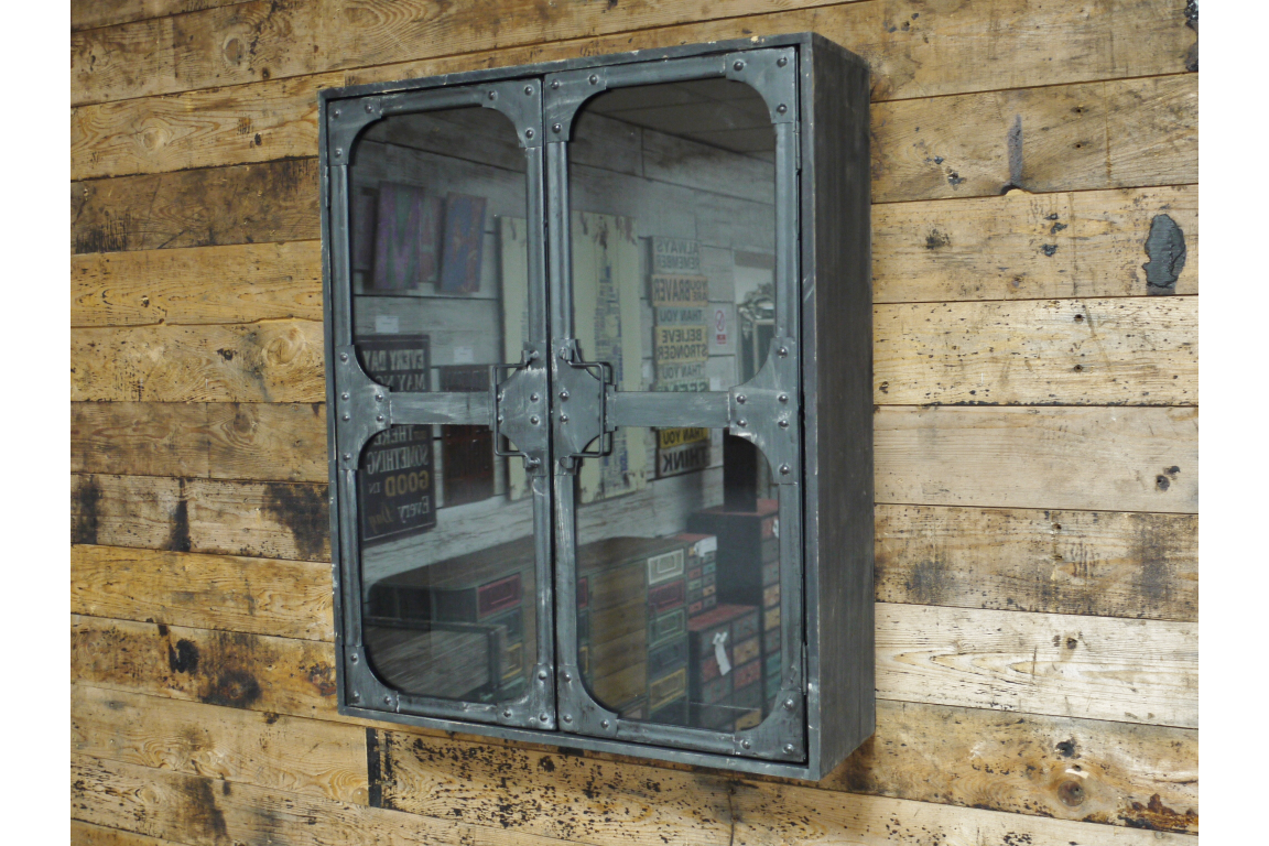 Metal wall cabinet with glass double doors, rivet details, mounted on rustic wooden plank wall, angled view.