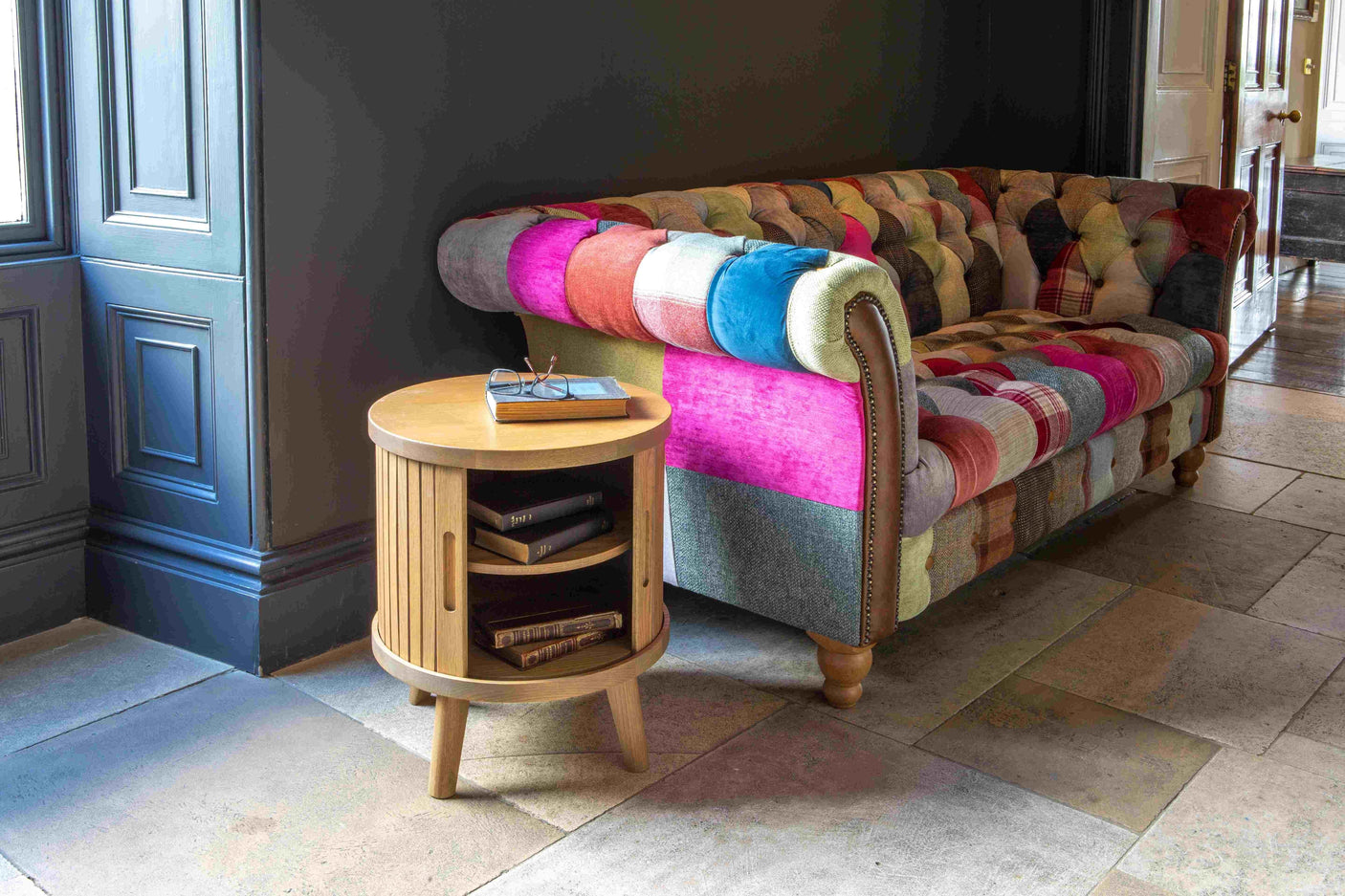 Patchwork fabric sofa with tufted design beside round wooden side table with books