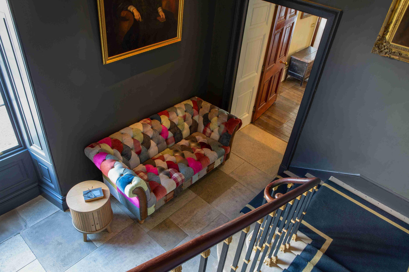 Patchwork fabric sofa with rolled arms in hallway corner beside round wooden side table
