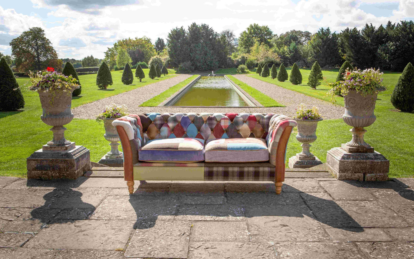 Patchwork fabric sofa with tufted backrest on stone patio outdoors near garden pond