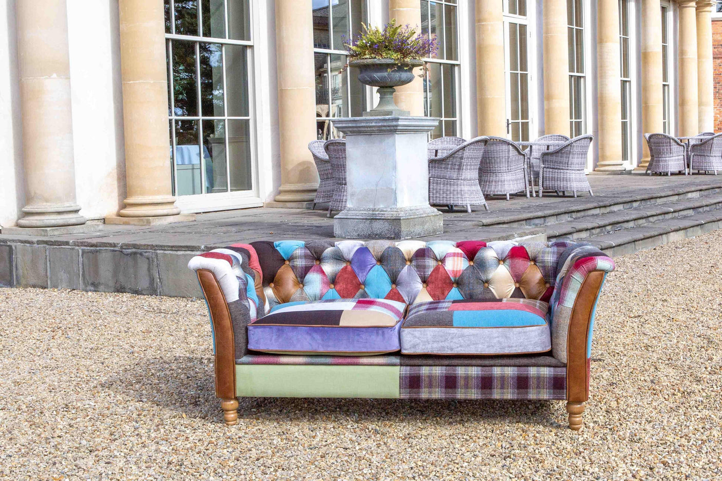 Patchwork fabric sofa with wooden legs on gravel patio outside classic building