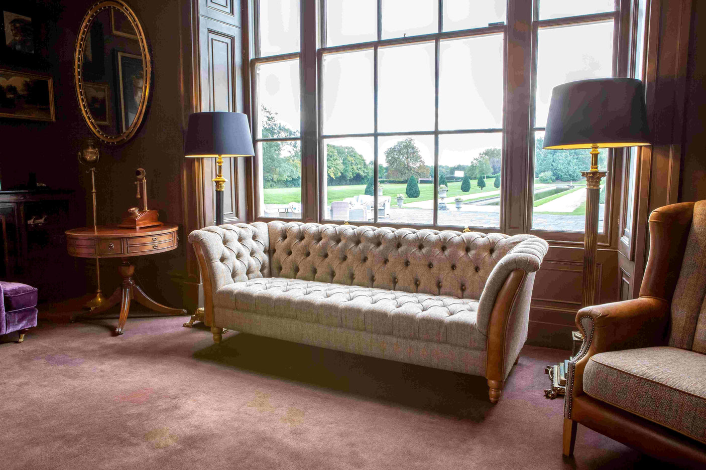 Tufted grey fabric chesterfield sofa in elegant living room with large window and wooden accents