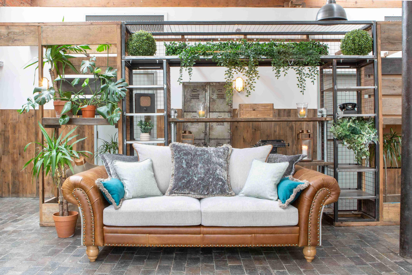 Tan leather sofa with light cushions in loft living room, surrounded by potted plants and shelving