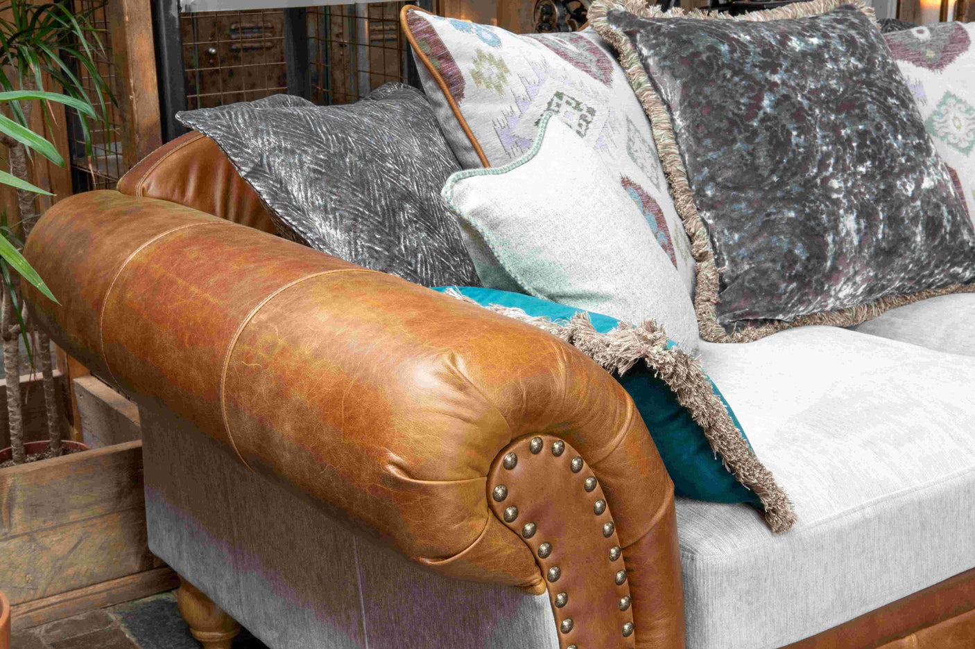 Brown leather and fabric sofa with studded armrest and assorted decorative cushions