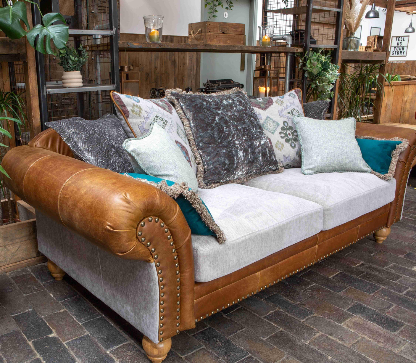 Brown leather and grey fabric sofa with studded arms, patterned cushions in rustic room