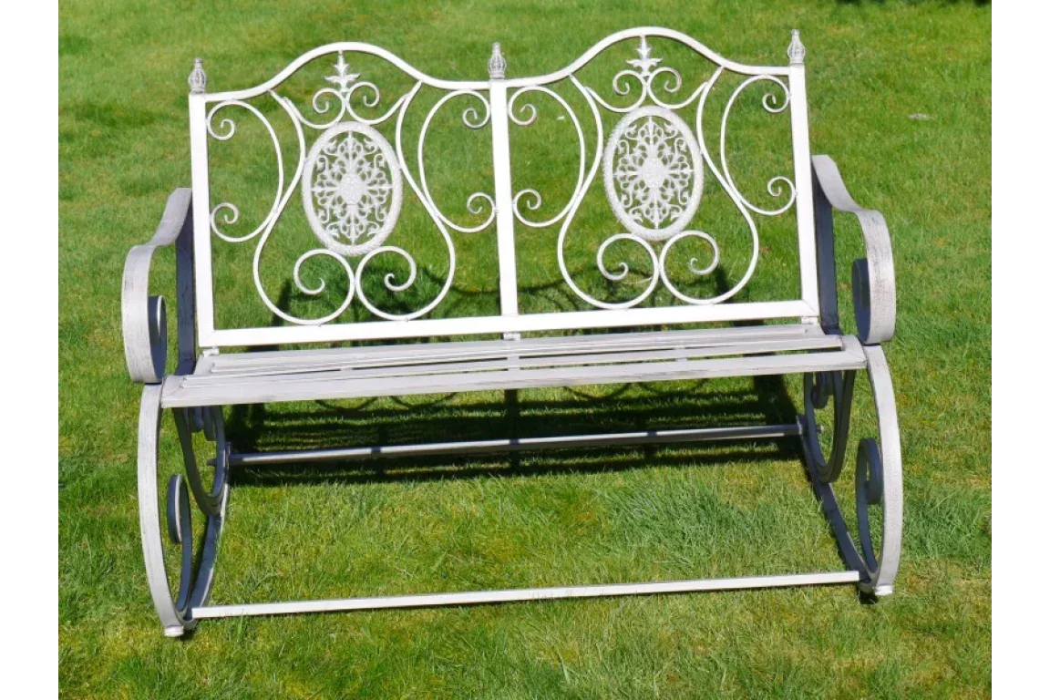 Decorative white metal garden bench with ornate backrest on grass lawn