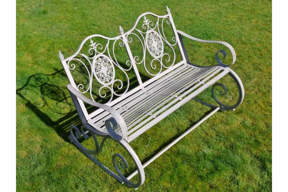 metal garden bench with decorative scrollwork backrest and slatted seat on grass