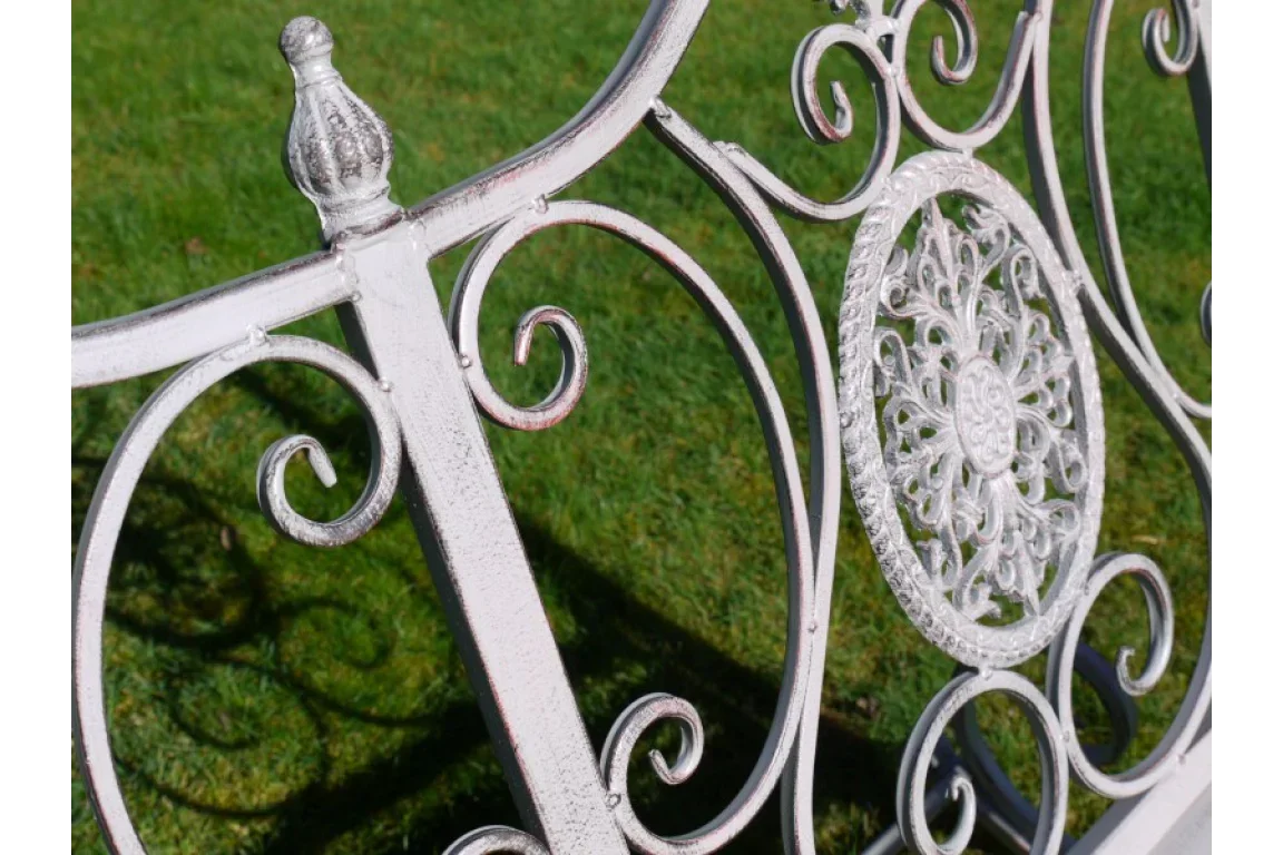 White metal garden bench with decorative scrollwork and floral detail on lawn