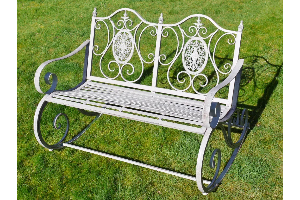 White wrought iron garden bench with ornate scrollwork on grass