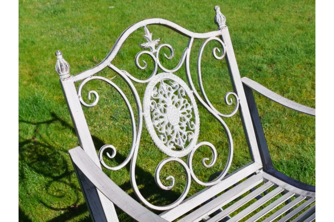 White metal garden bench with ornate floral backrest on green lawn