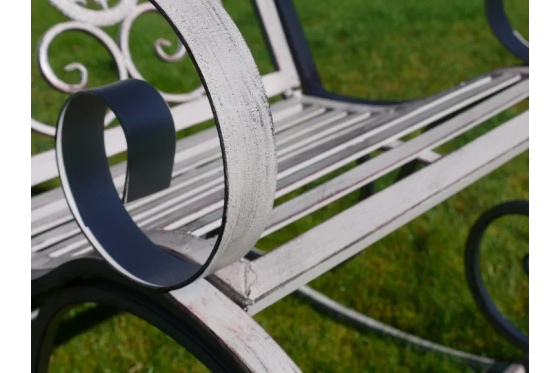 Close up of white metal garden bench with scroll armrest on lawn