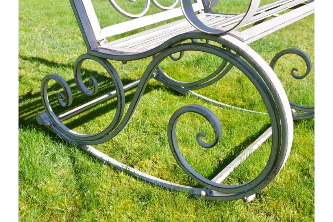 Metal garden rocking bench with ornate scrollwork detail on grass lawn