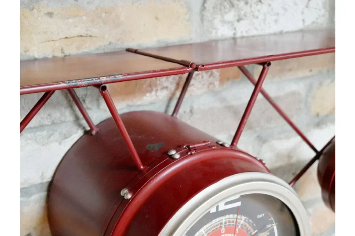 Red metal clock shelf with airplane wing design against brick wall