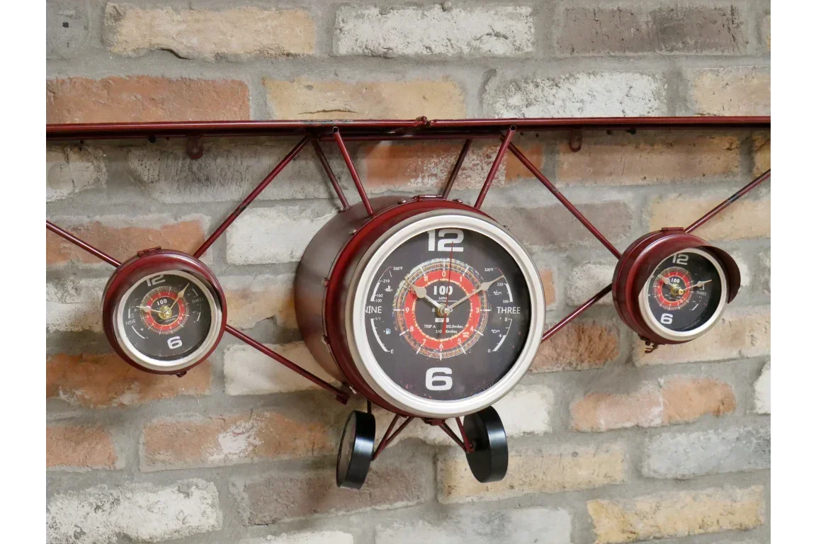 Red metal airplane wall clock with three dials on exposed brick background