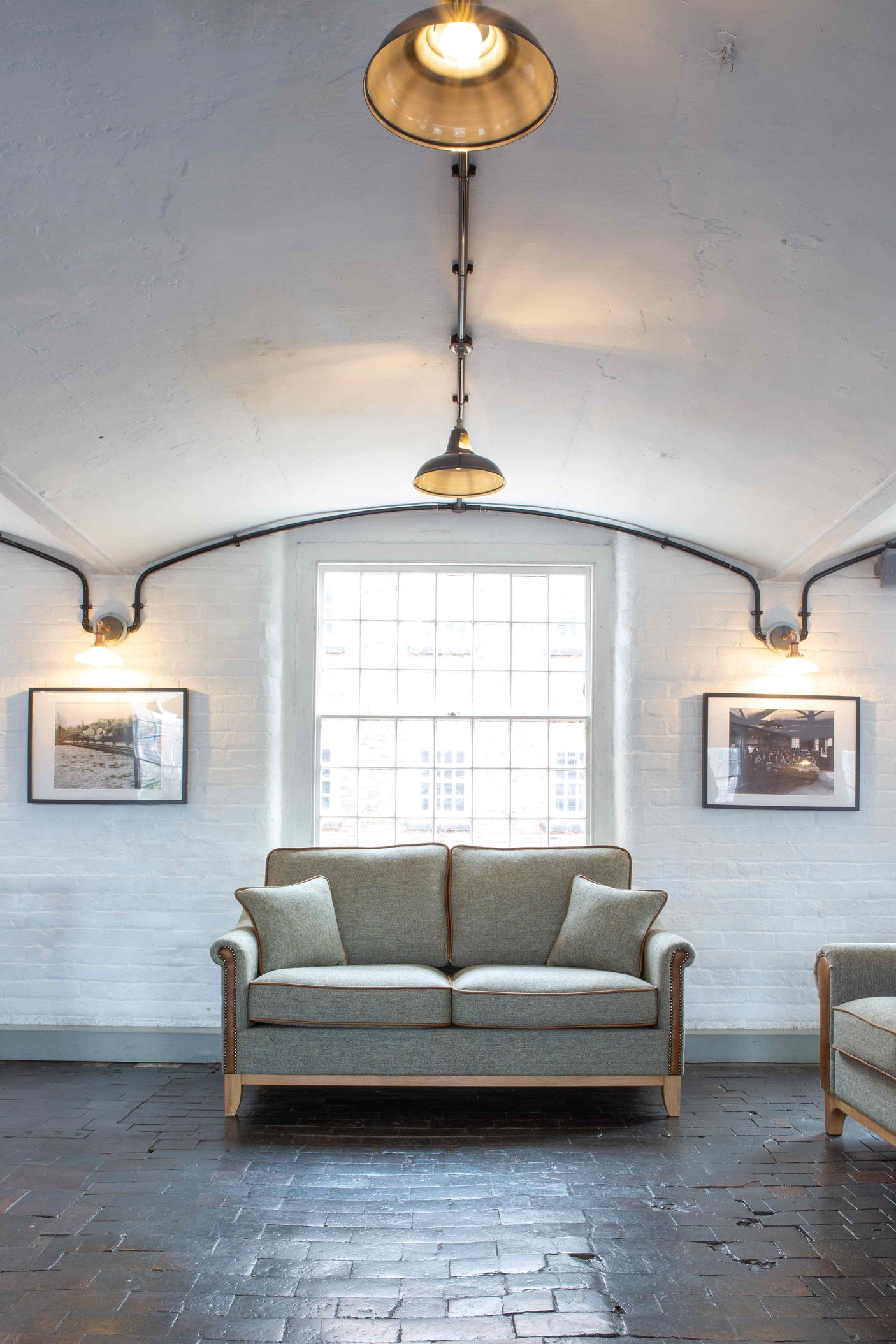 Grey fabric sofa with wooden legs in front of window, brick wall, and framed photos