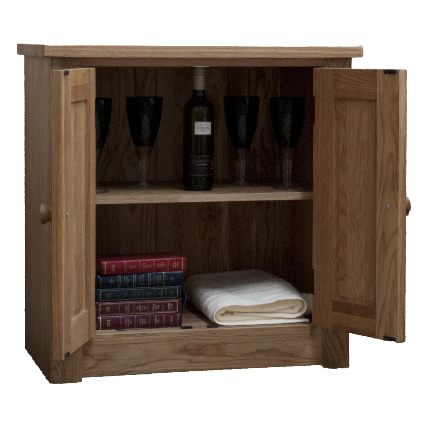 Oak sideboard cabinet with open doors, shelves holding wine glasses, bottle, books, towel
