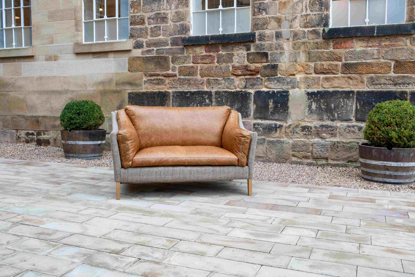 Tan leather two-seater sofa with wooden legs on stone patio, outdoor setting
