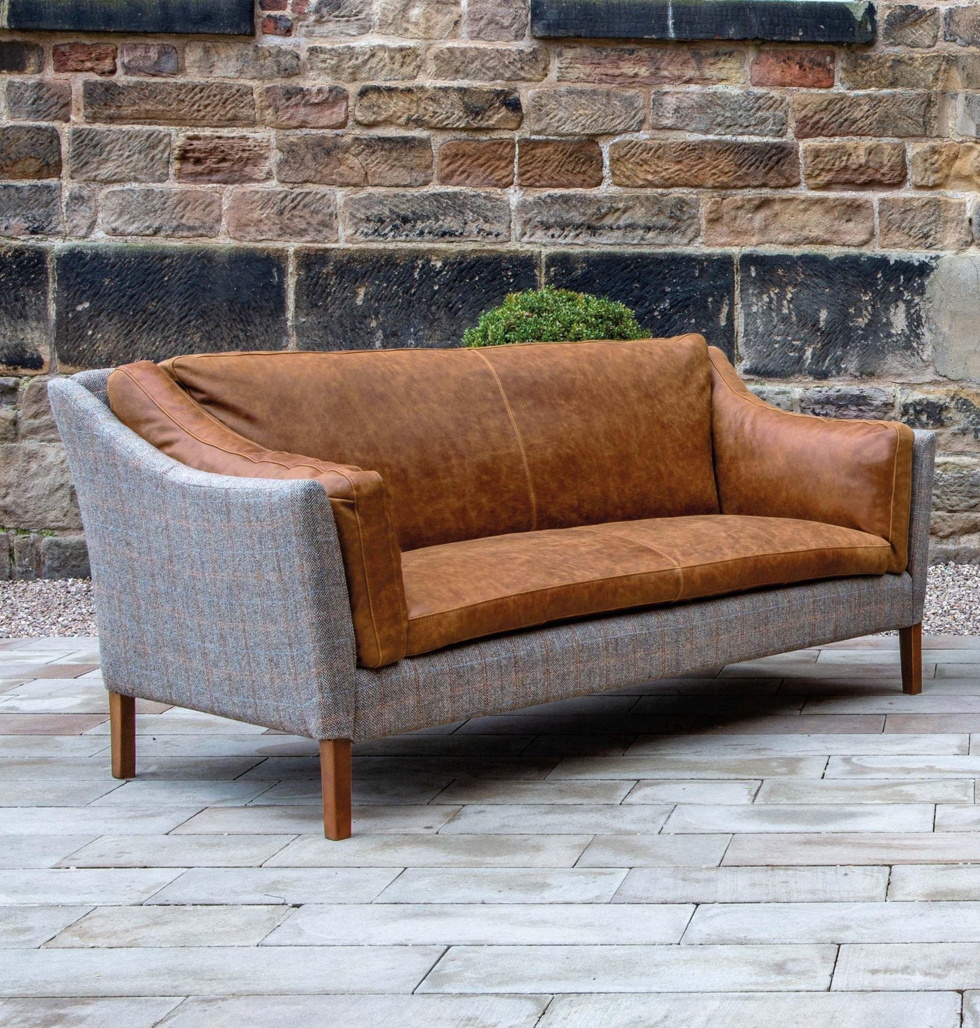 Brown leather and grey fabric sofa with wooden legs on patio