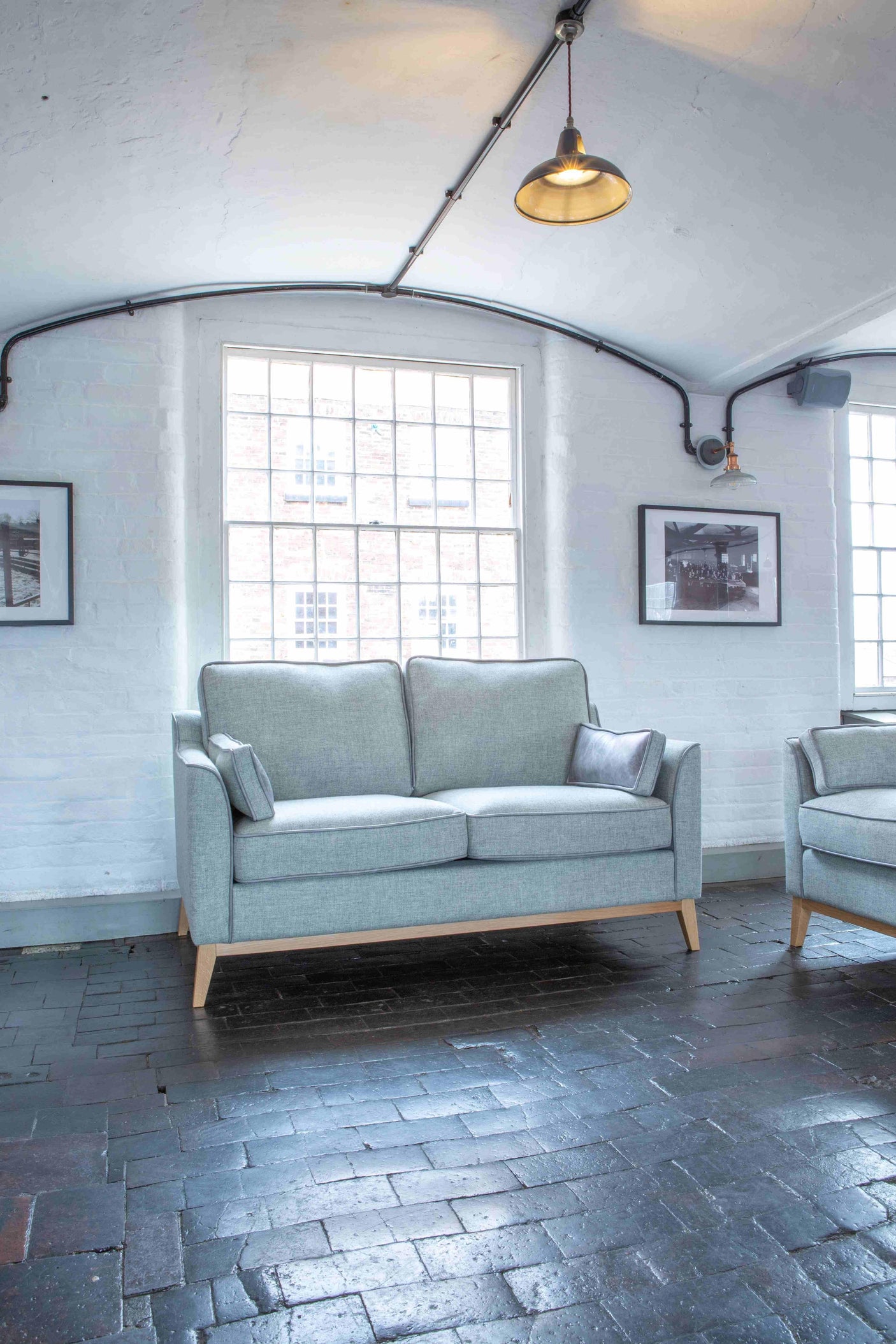 Light grey fabric sofa with wooden legs placed in a modern living room with large window