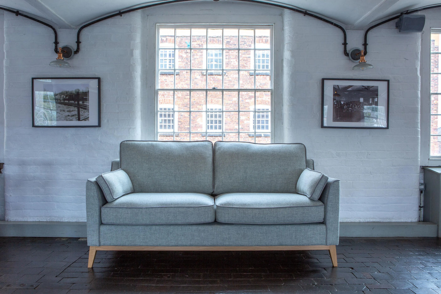 Light grey fabric sofa with wooden legs in modern living room with tall windows
